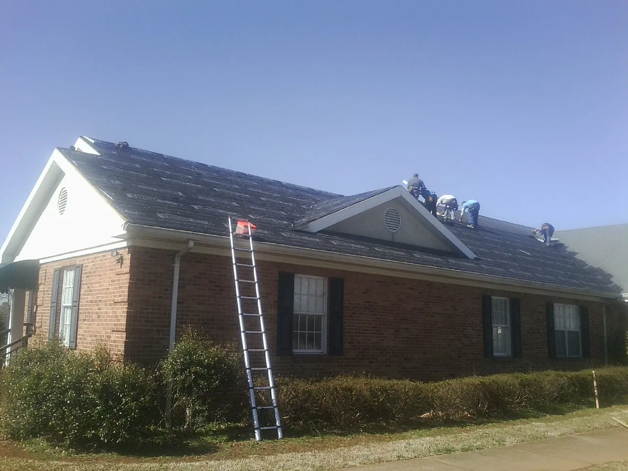 Crew tearing shingles off a brick ranch roof with a ladder set — Metal Roof Repair work by our crew in Endicott