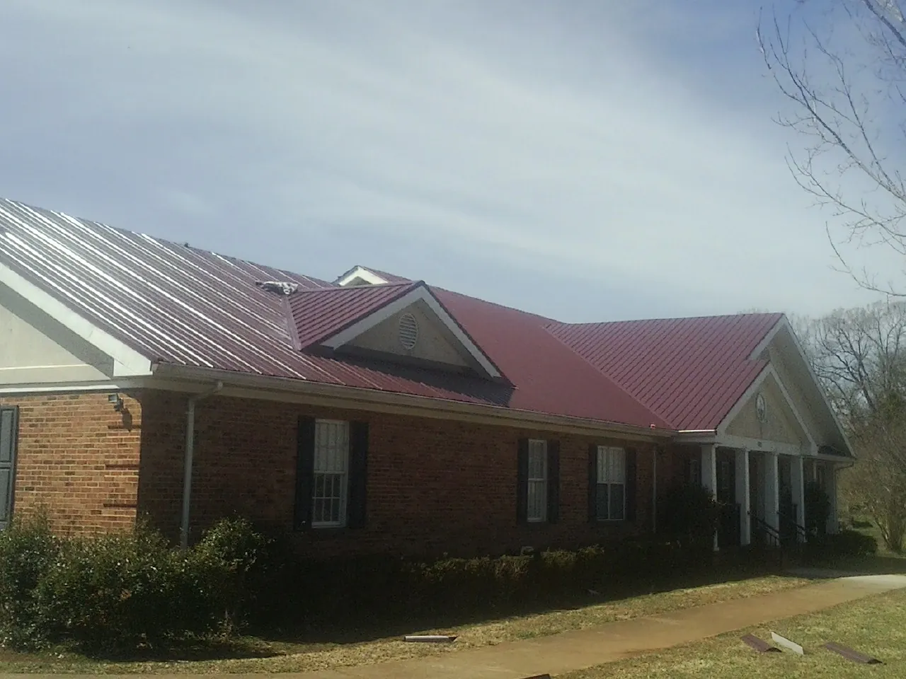 Red metal roof with gabled entries on a long brick building, from a Hail Damage Roof Repair job in Endicott