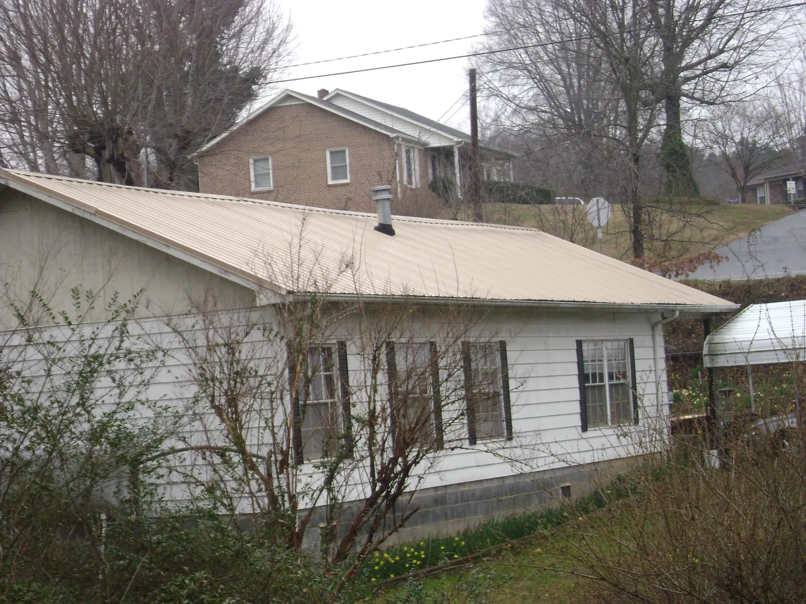 Tan metal roof on a white sided house set into a hillside — Commercial Roofing by Roofing Brothers in Endicott